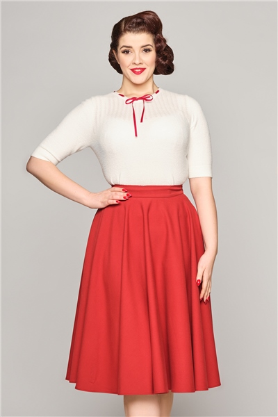 Femme souriante portant une jupe swing rouge et un haut à manches courtes blanc.