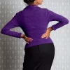 Femme en pull violet de dos avec les mains sur les hanches, regardant par-dessus son épaule.
