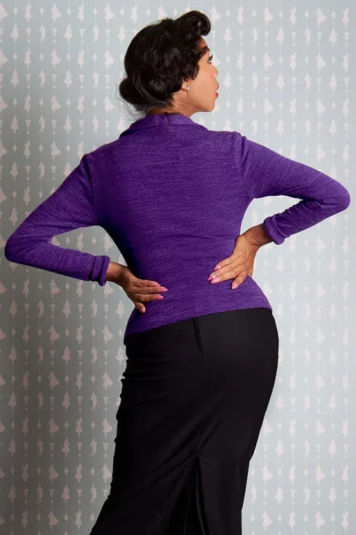 Femme en pull violet de dos avec les mains sur les hanches, regardant par-dessus son épaule.