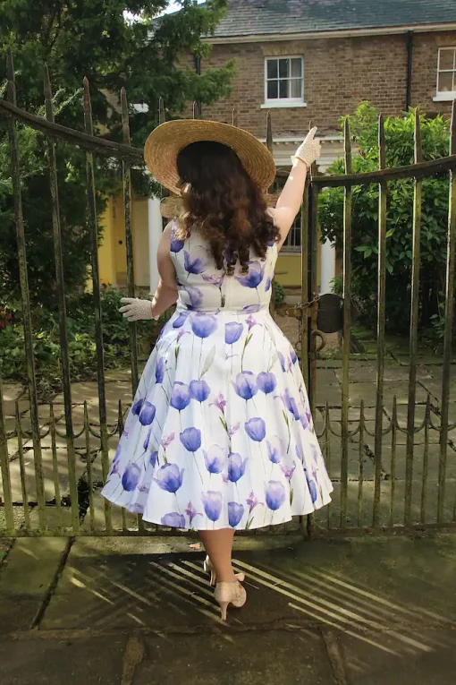 Vue arrière d'une femme portant la Robe Swing Florale Cathy, tenant un chapeau de paille, avec des iris bleus et violets imprimés.